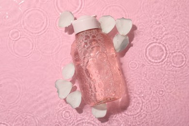 Photo of Wet bottlemicellar water and petals on pink background, top view