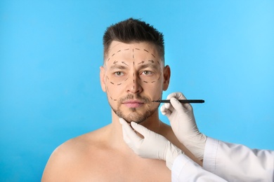 Doctor drawing marks on man's face for cosmetic surgery operation against blue background