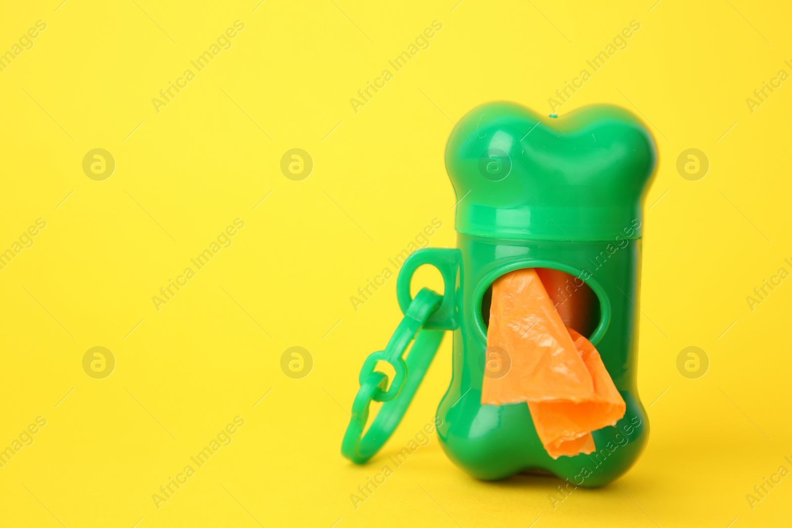 Photo of Dispenser with dog waste bags on yellow background. Space for text