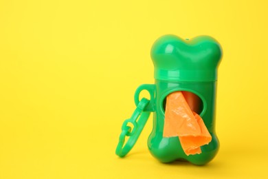Dispenser with dog waste bags on yellow background. Space for text
