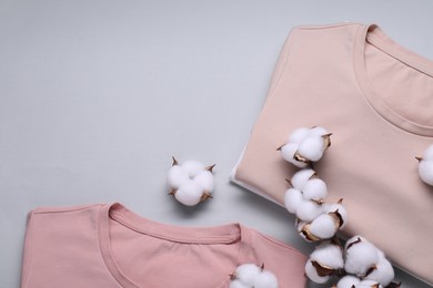 Photo of Cotton branch with fluffy flowers and t-shirts on light gray background, flat lay. Space for text