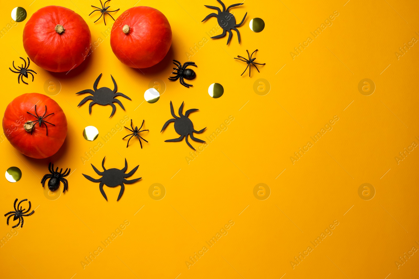 Photo of Flat lay composition with pumpkins, spiders and golden confetti on yellow background, space for text. Halloween celebration