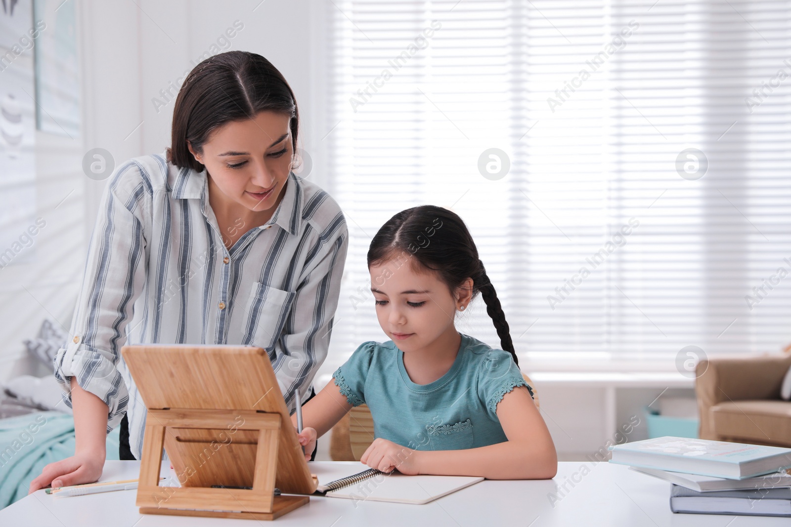 Photo of Mother helping her daughter doing homework with tablet at home