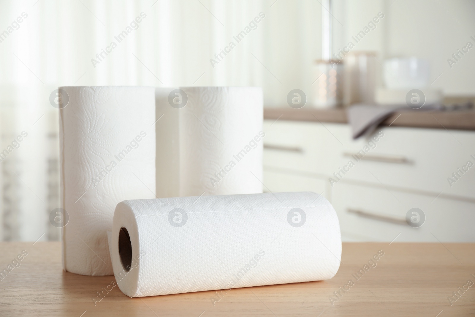 Photo of Rolls of paper towels on wooden table in kitchen. Space for text