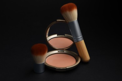 Photo of Open face powder with mirror and makeup brushes on black background