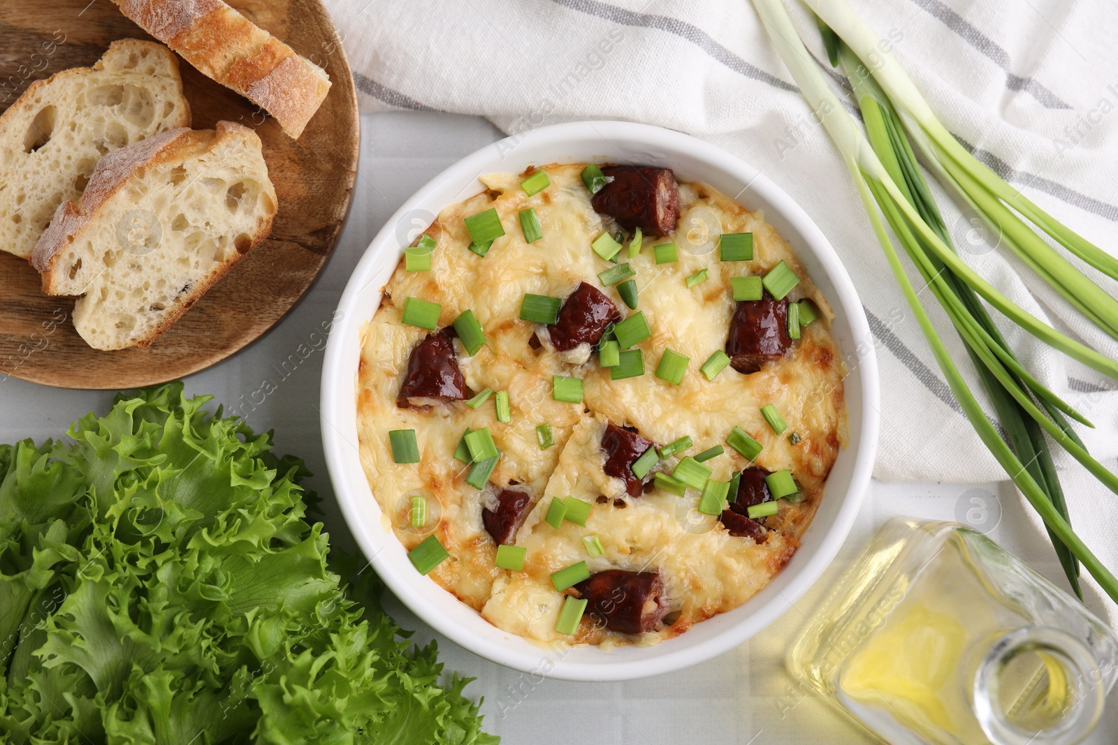 Photo of Tasty sausage casserole in baking dish served on white tiled table, flat lay