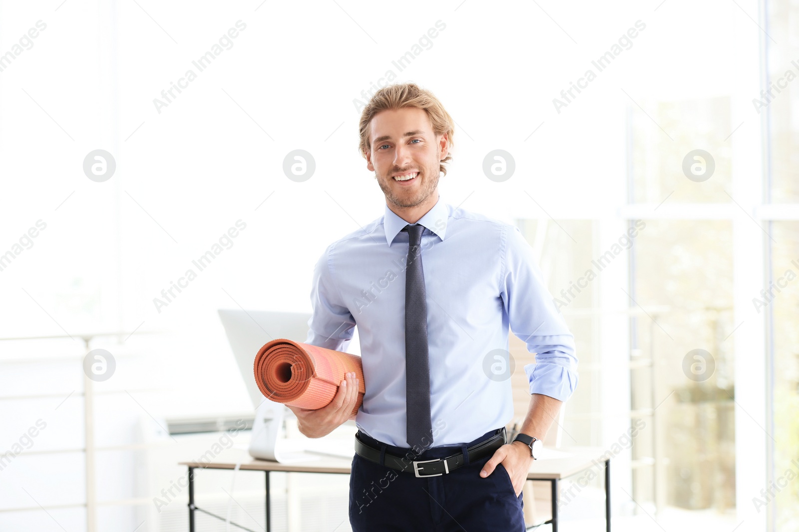 Photo of Young handsome businessman holding yoga mat in office. Gym after work