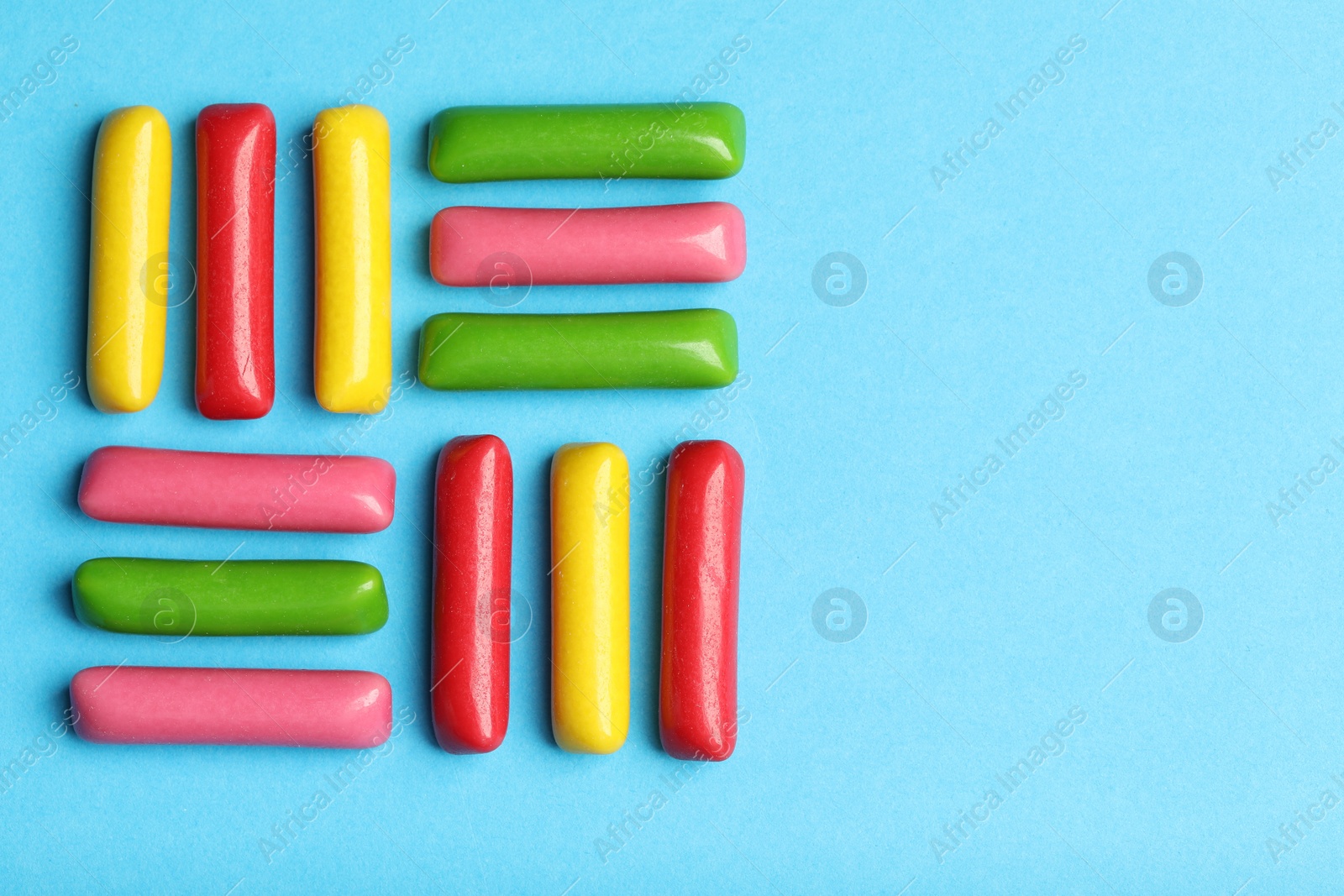 Photo of Many tasty bubble gums on light blue background, flat lay. Space for text