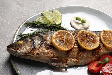 Photo of Delicious roasted sea bass fish served with lemon, rosemary and sauce on light grey table, closeup