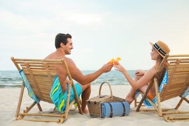 Happy young couple with cocktails sitting on deck chairs at sea beach