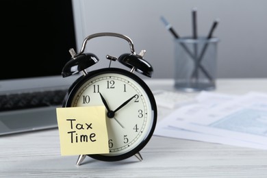 Photo of Alarm clock and reminder note with words Tax Time on white wooden table. Space for text