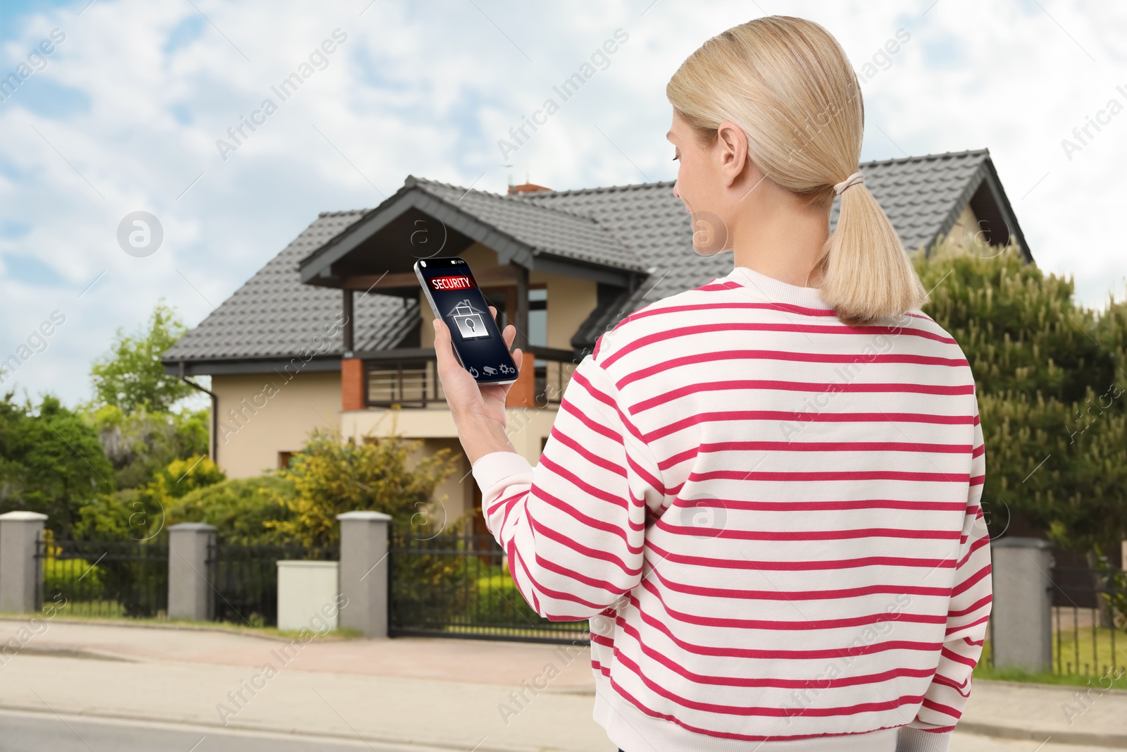 Image of Woman using home security system application on smartphone outdoors