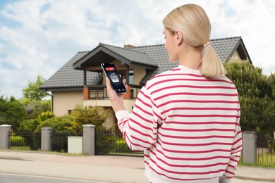 Woman using home security system application on smartphone outdoors