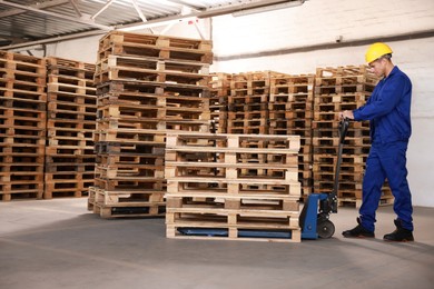 Image of Worker moving wooden pallets with manual forklift in warehouse