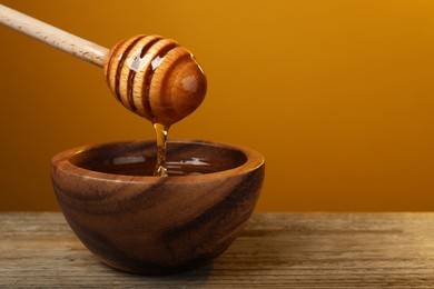 Photo of Pouring honey from dipper into bowl at wooden table against golden background, space for text