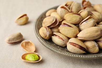 Photo of Plate and pistachio nuts on beige tablecloth, closeup