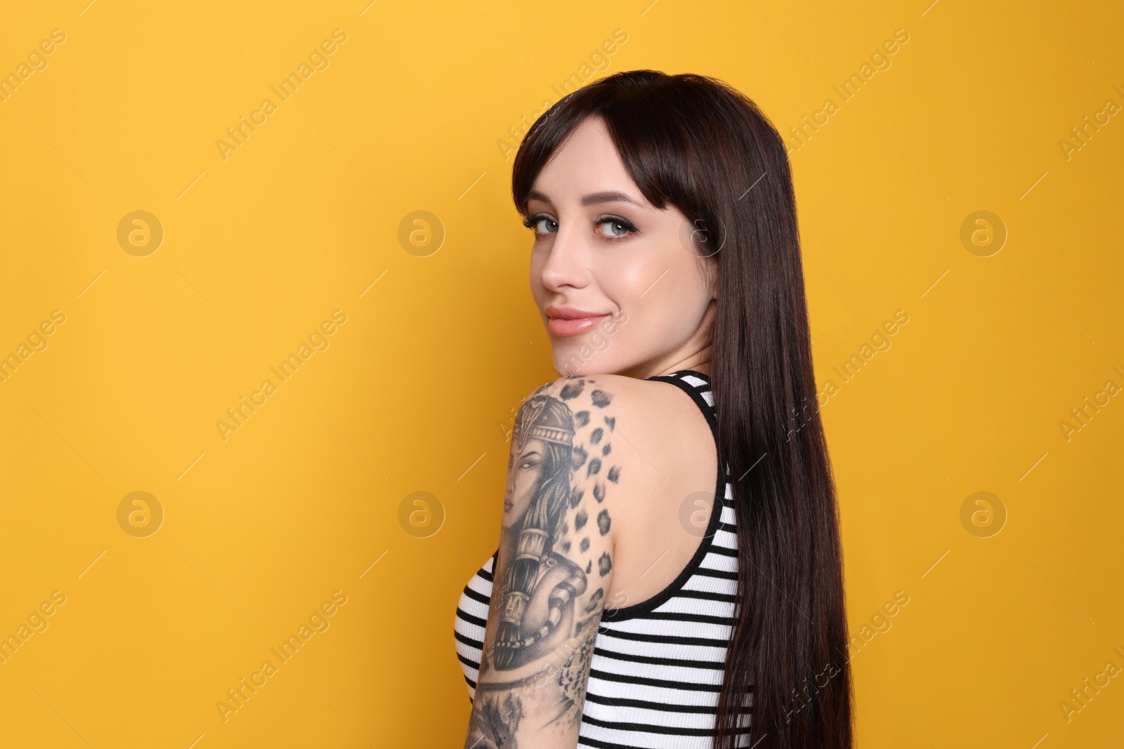 Photo of Beautiful woman with tattoos on arm against yellow background. Space for text