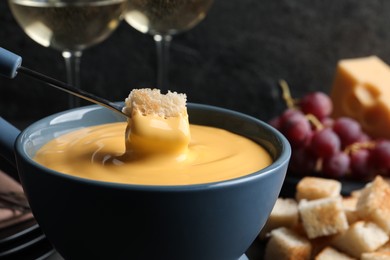 Dipping piece of bread into tasty cheese fondue, closeup