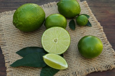 Photo of Fresh ripe limes and green leaves on wooden table