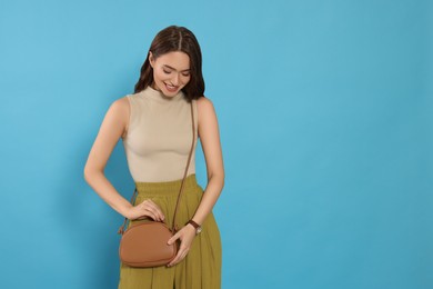 Beautiful young woman in fashionable outfit with stylish bag on light blue background, space for text