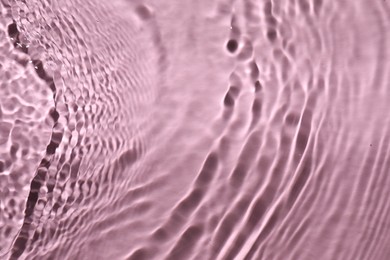 Rippled surface of clear water on pink background, top view