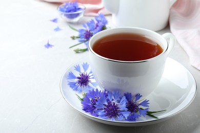 Photo of Cup of tea and cornflowers on light table, closeup. Space for text