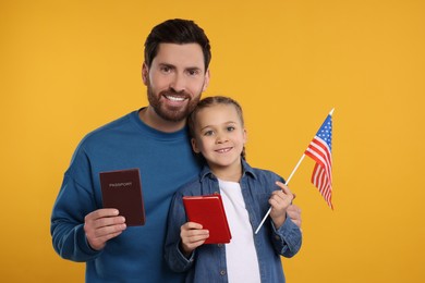 Immigration. Happy man with his daughter holding passports and American flag on orange background