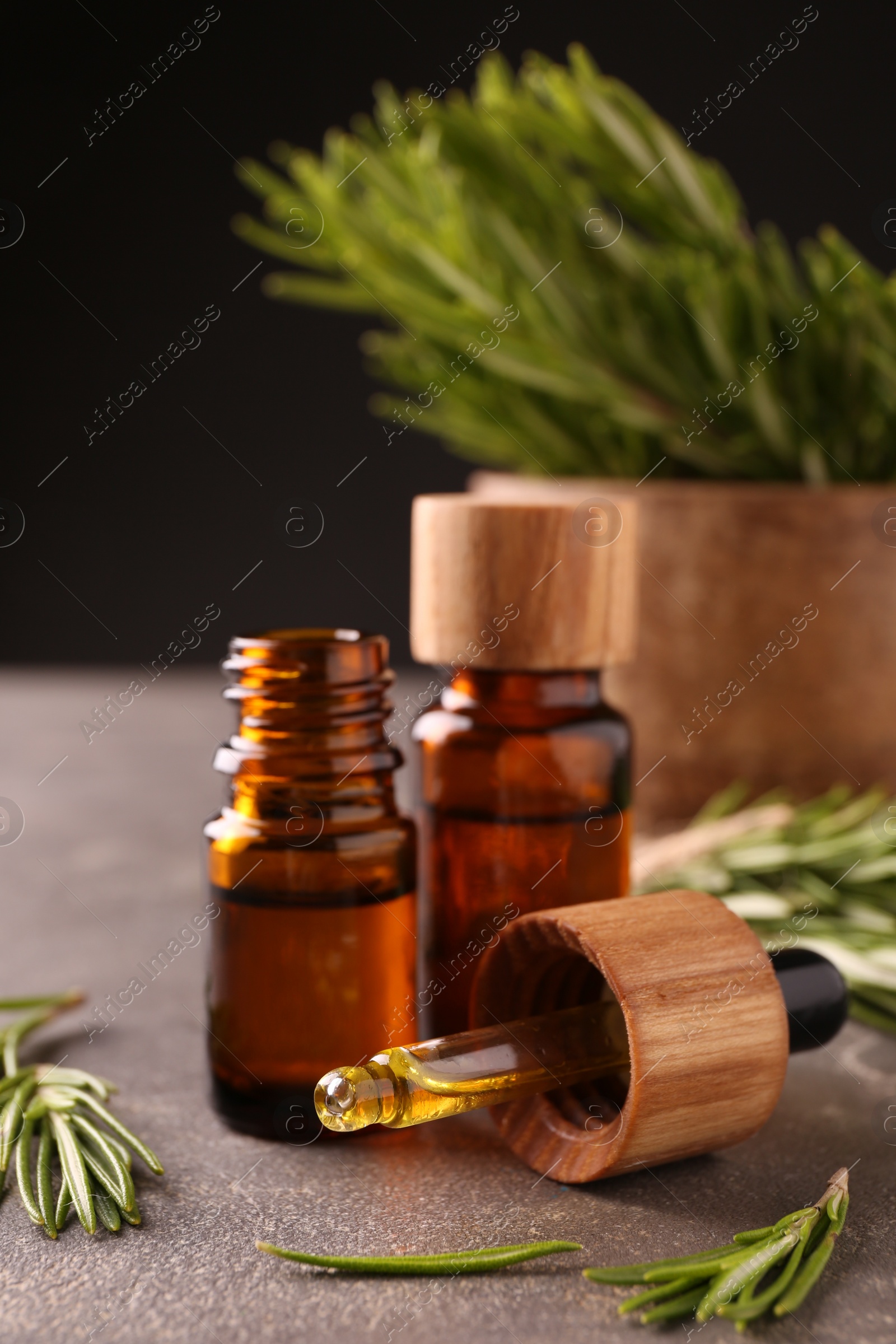 Photo of Essential oil in bottles, dropper and rosemary on grey table