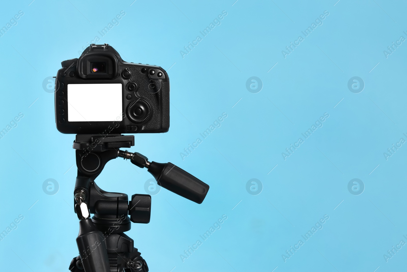 Photo of Modern tripod with professional camera on light blue background. Space for text