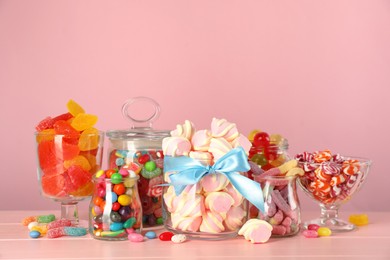 Photo of Jars with different delicious candies on pink wooden table