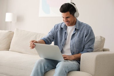 Photo of Man with laptop and headphones sitting on sofa at home