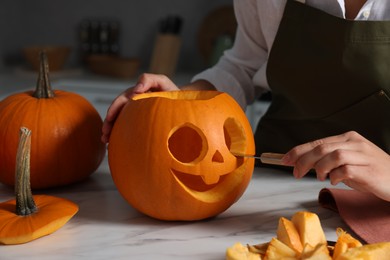 Woman carving pumpkin for Halloween at white marble table in kitchen, closeup