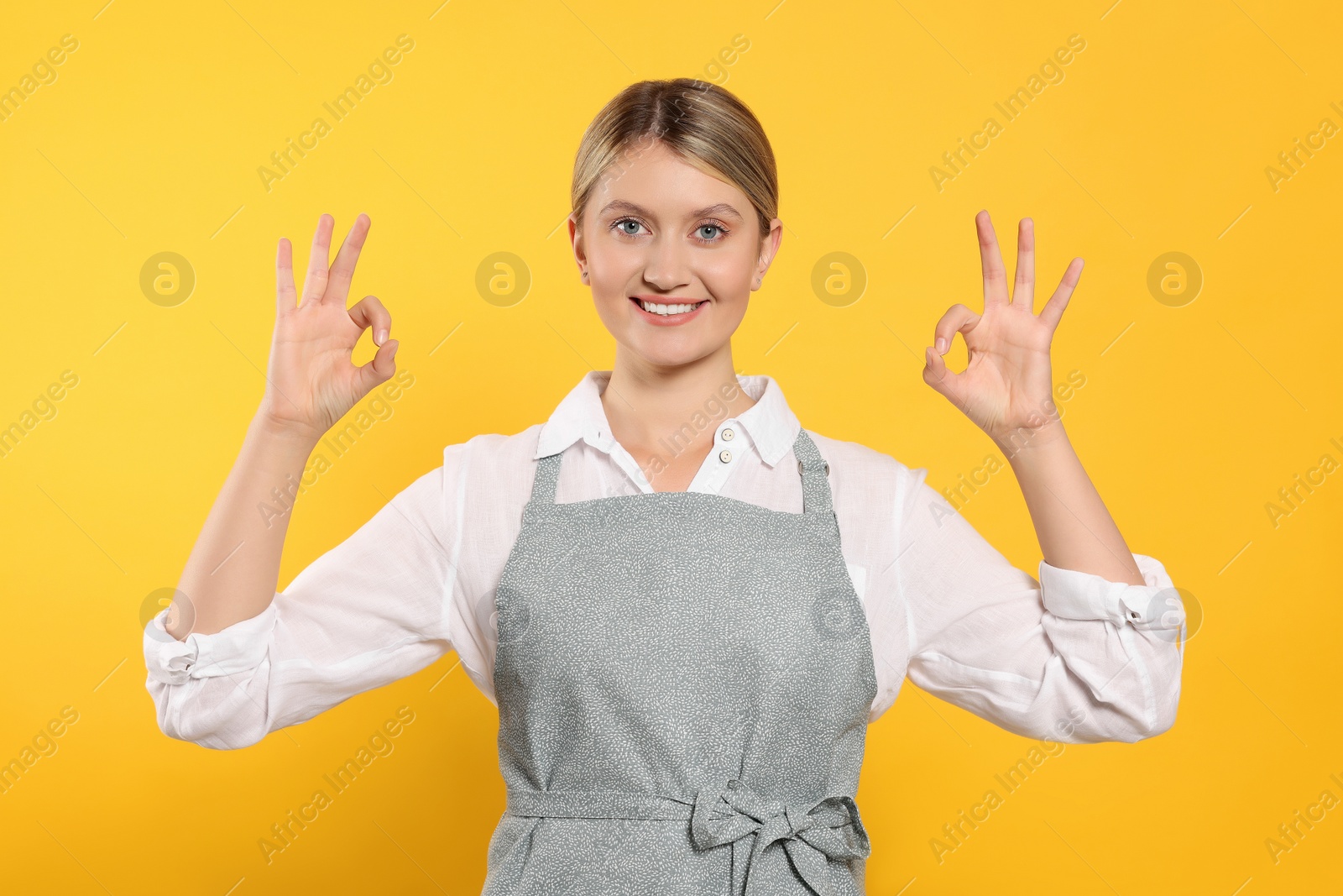 Photo of Beautiful young woman in clean apron with pattern on orange background