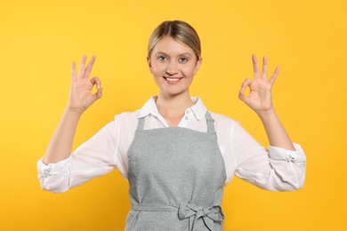 Beautiful young woman in clean apron with pattern on orange background