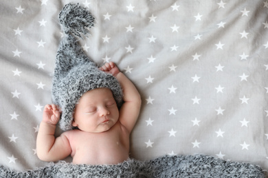 Cute newborn baby in warm hat sleeping on bed, top view. Space for text