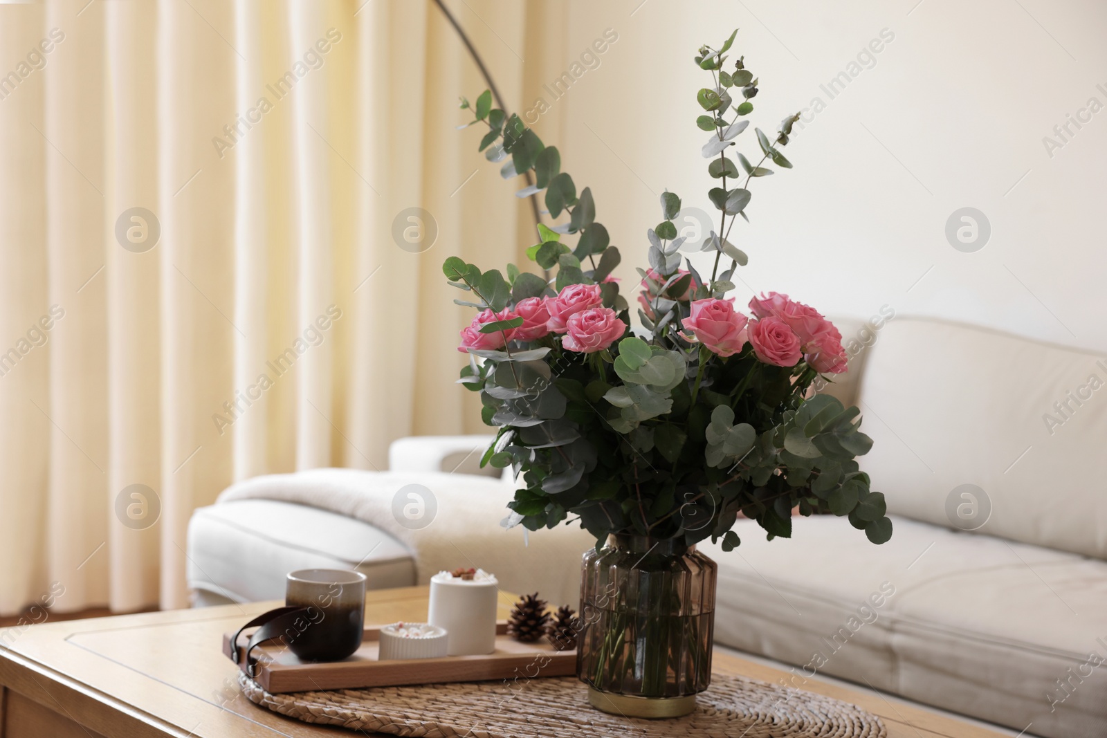 Photo of Beautiful bouquet of roses and eucalyptus branches in vase near candles on table at home. Space for text