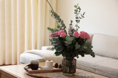 Photo of Beautiful bouquet of roses and eucalyptus branches in vase near candles on table at home. Space for text