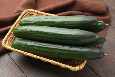 Fresh cucumbers in wicker basket on wooden table, closeup