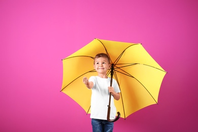 Photo of Little boy with yellow umbrella on color background