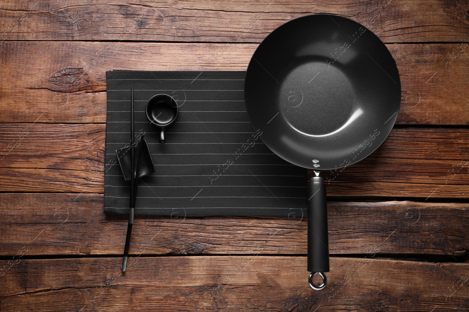 Photo of Empty iron wok, sauce bowl and chopsticks on wooden table, flat lay