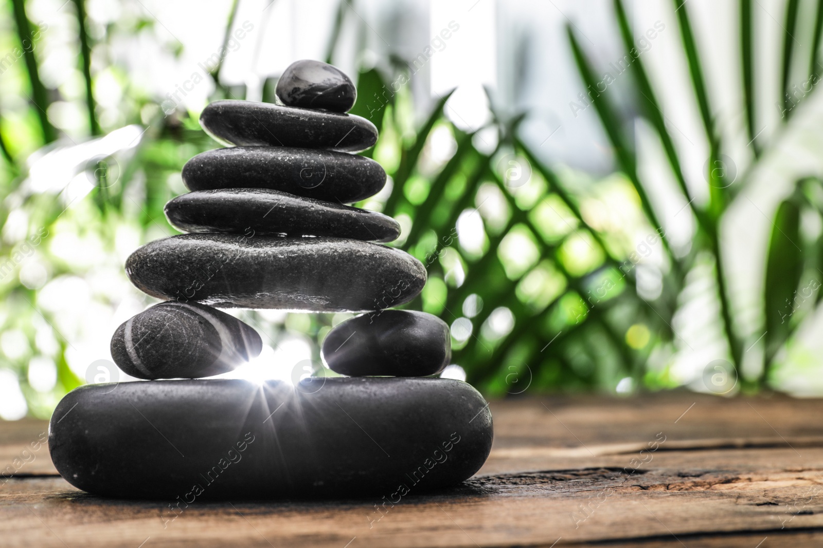 Photo of Table with stack of stones and blurred green leaves on background, space for text. Zen concept