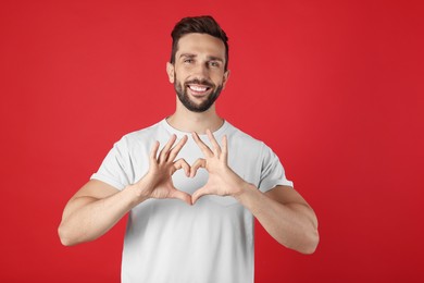 Photo of Happy man making heart with hands on red background