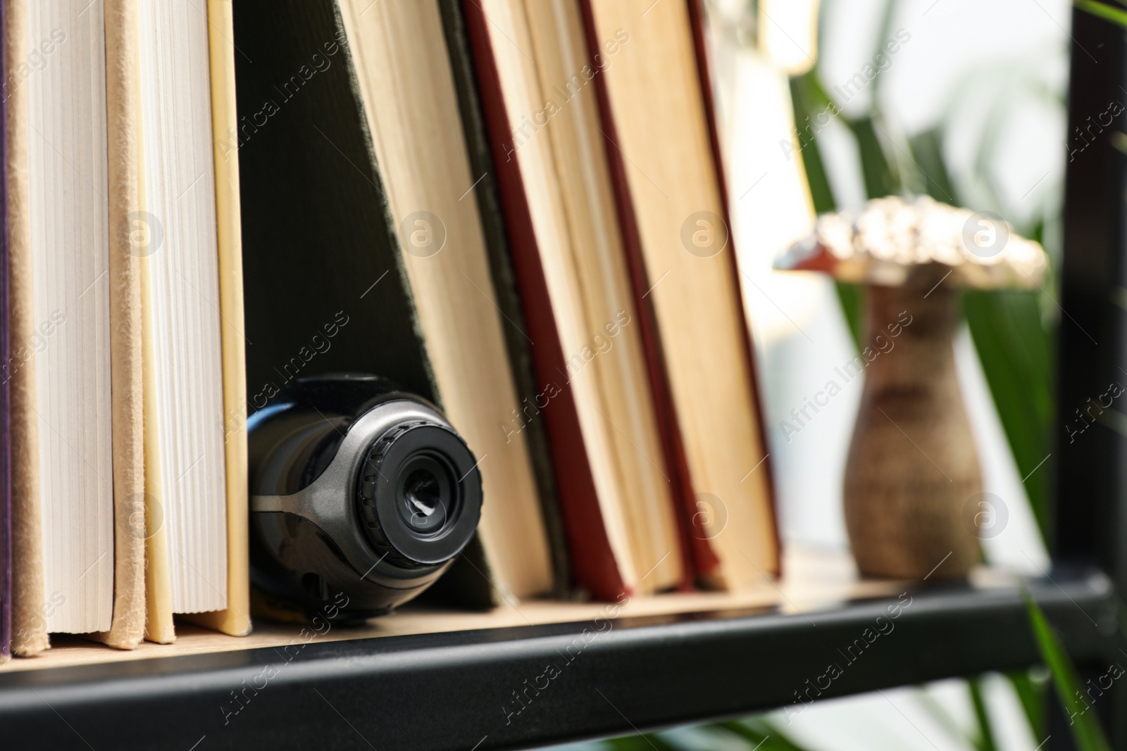 Photo of Camera hidden between books on wooden shelf indoors, closeup. Space for text