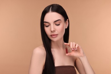 Photo of Beautiful young woman holding skincare ampoule on beige background