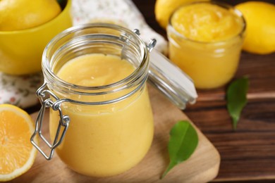 Delicious lemon curd in glass jars, fresh citrus fruits and green leaves on wooden table, closeup