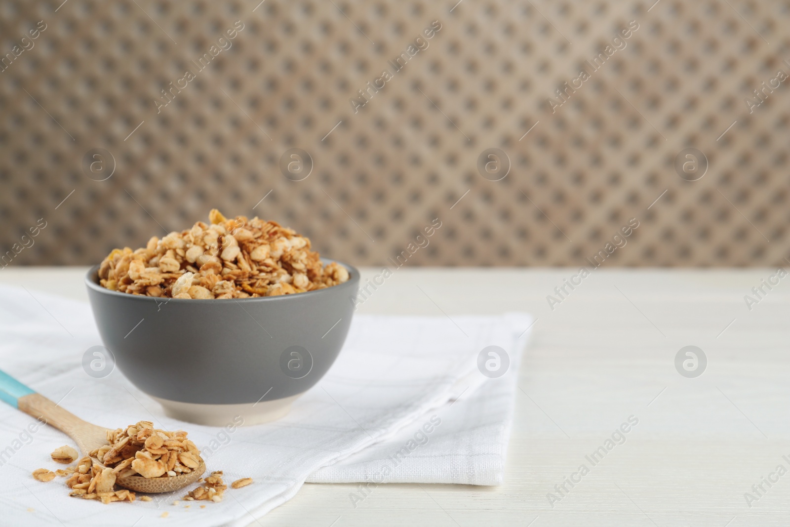 Photo of Ceramic bowl with granola on white wooden table, space for text. Cooking utensil