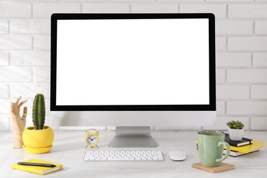 Photo of Office workplace with computer, stationery, cup and houseplants on light table near white brick wall