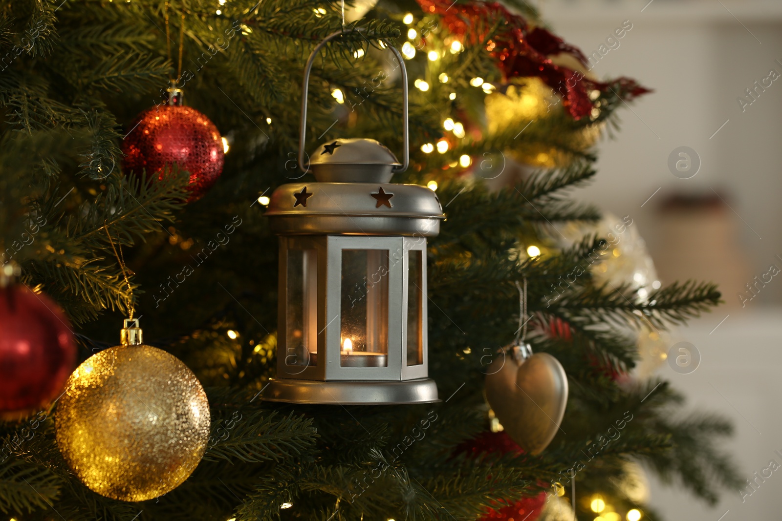 Photo of Christmas lantern with burning candle and balls on fir tree indoors, closeup