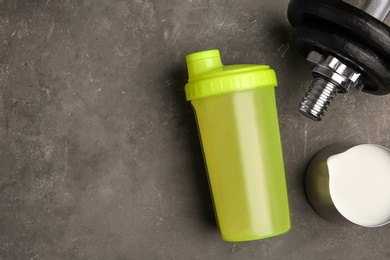 Photo of Bottle with protein shake, jug of milk and dumbbell on grey background, top view. Space for text