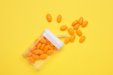 Photo of Tasty dragee candies and container on yellow background, flat lay